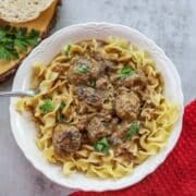 swedish meatballs over egg noodles in a white plate with a red napkin