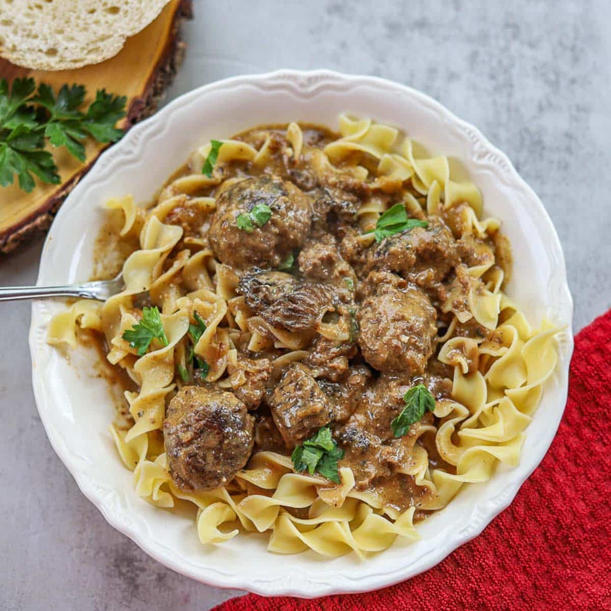 swedish meatballs over egg noodles in a white plate with a red napkin