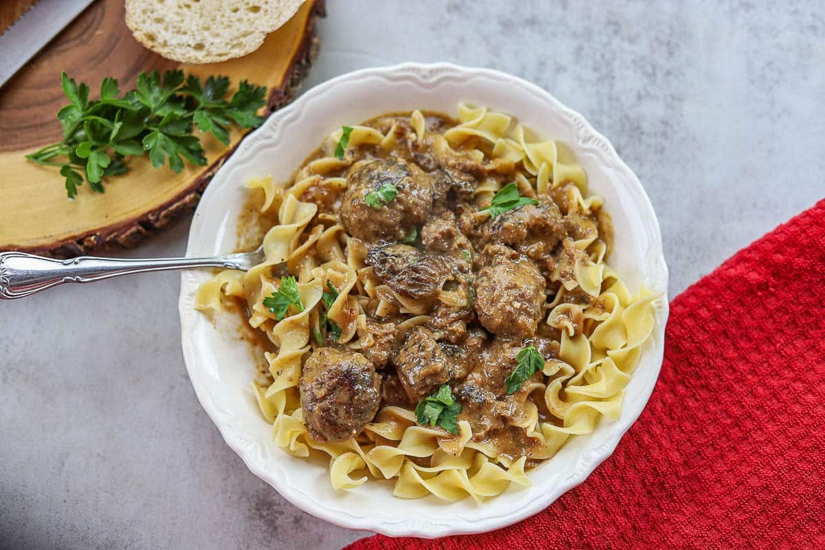 swedish meatballs over egg noodles in a white plate with a red napkin
