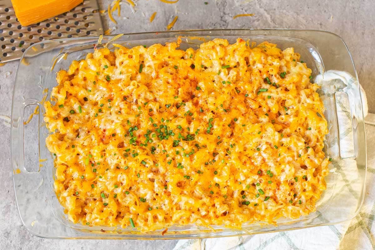 baked high protein mac and cheese in a sheet pan topped with fresh chives beside hand towel and cheese grater.
