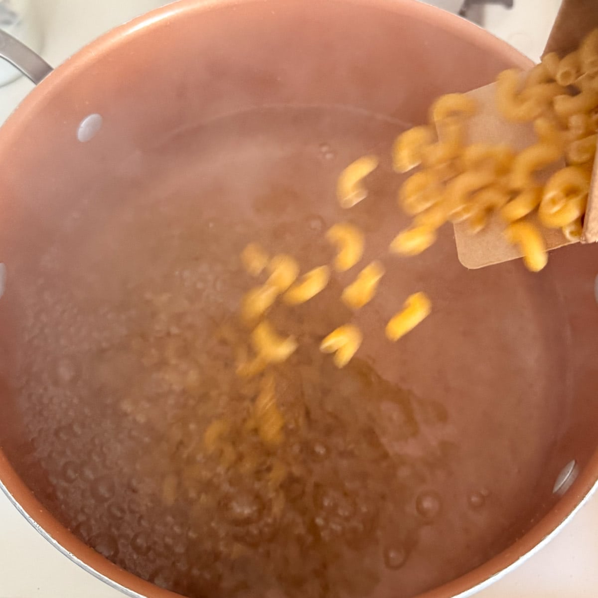 macaroni noodles being poured into a pot of boiling water.