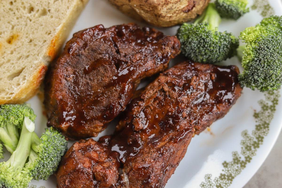 a white plate with slow cooker country style ribs with baked potato, broccoli, and sourdough bread