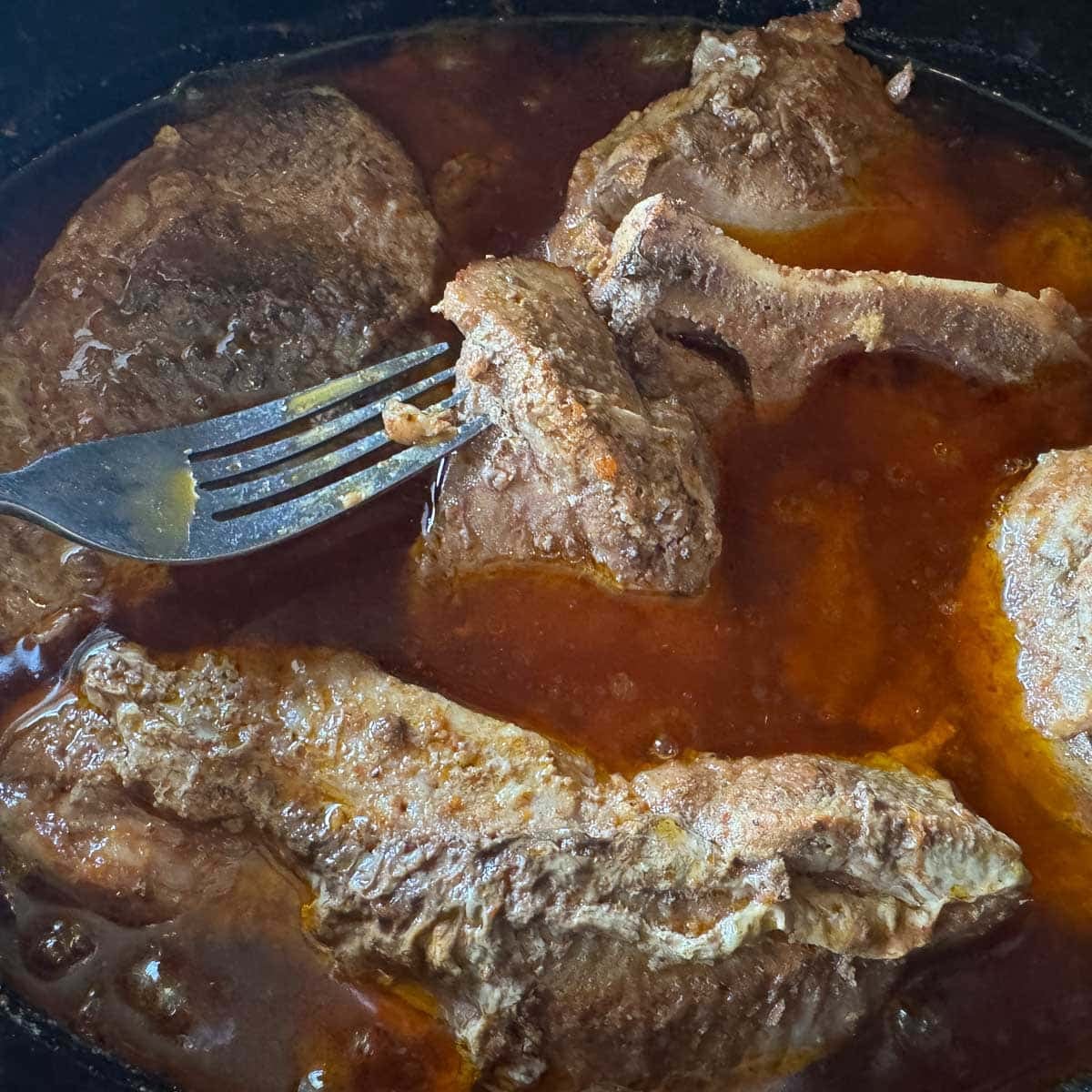 country style pork ribs in cooking juices with a fork checking for doneness