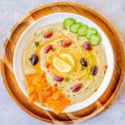 homemade hummus without tahini topped with kalamata olives, lemon, cucumbers, pita chips.