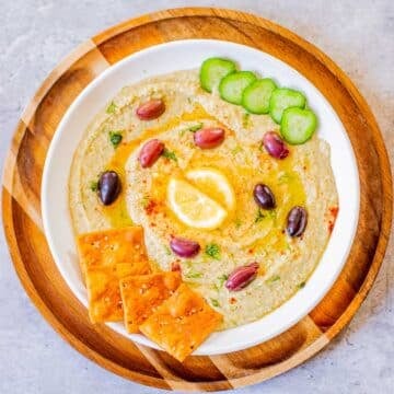 homemade hummus without tahini topped with kalamata olives, lemon, cucumbers, pita chips.