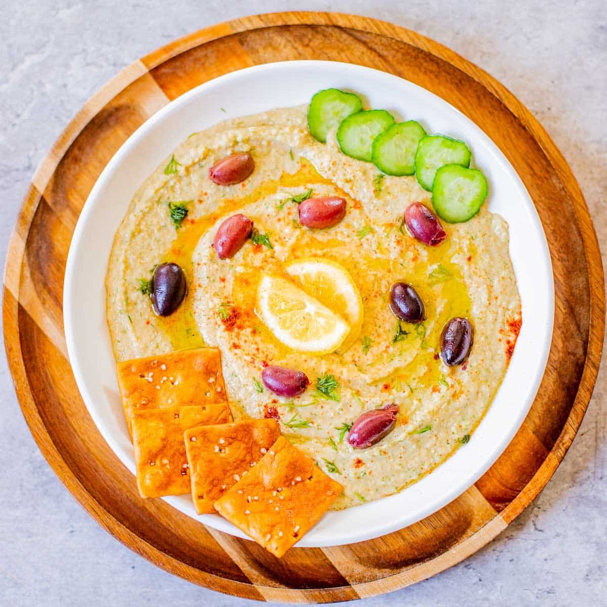 homemade hummus without tahini topped with kalamata olives, lemon, cucumbers, pita chips.