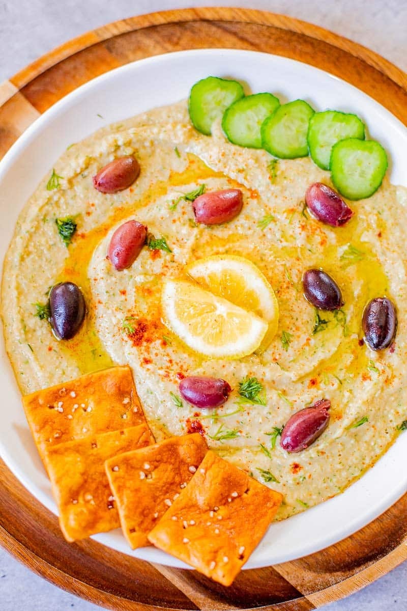 hummus recipe without tahini topped with kalamata olives, lemon, cucumbers, pita chips.