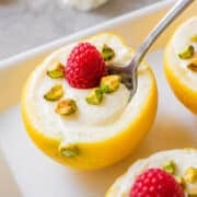 lemon posset in lemon skins with raspberries and pistachios and a spoon.
