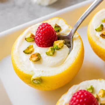 lemon posset in lemon skins with raspberries and pistachios and a spoon.