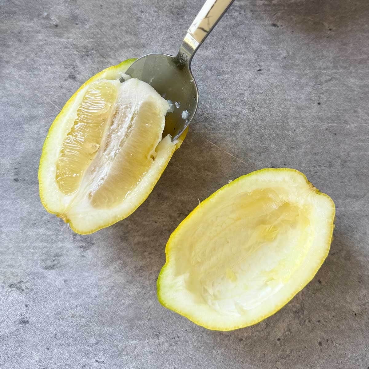 spoon scooping flesh out of halved lemon.