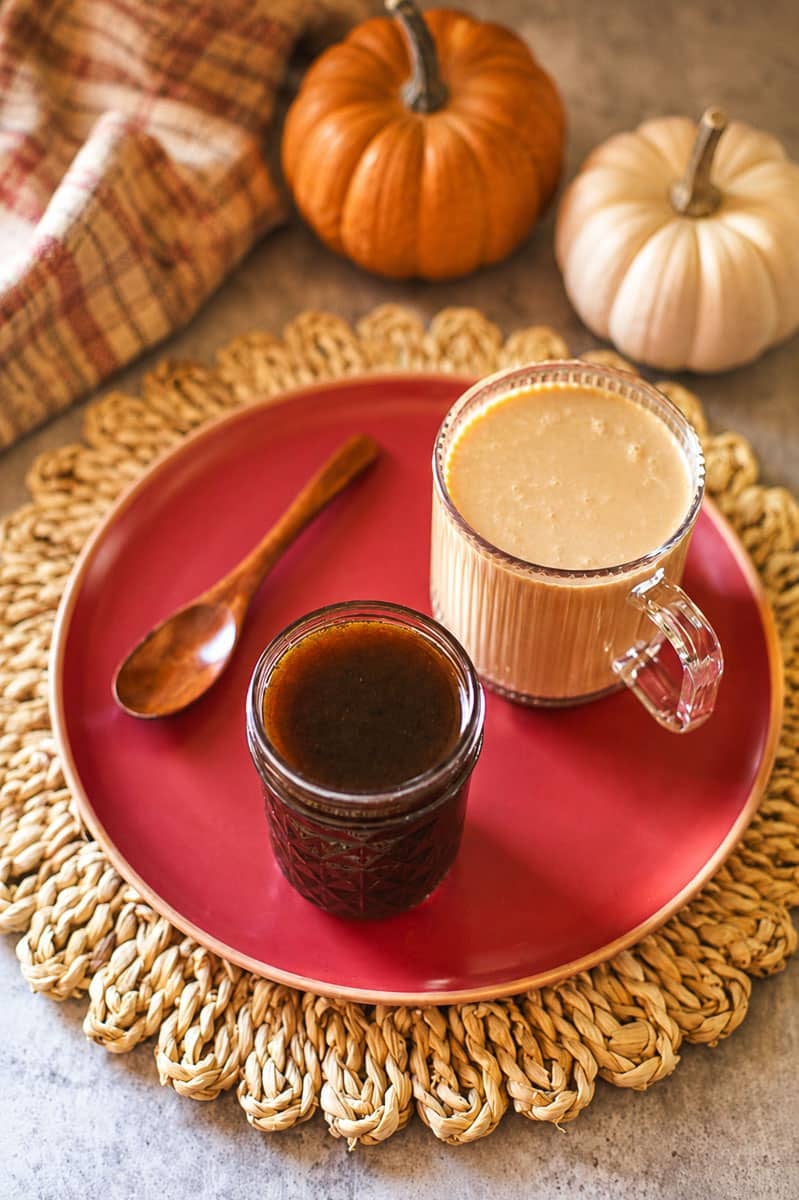 pumpkin spice coffee syrup in jar beside cup of coffee, wooden spoon, and pumpkins.