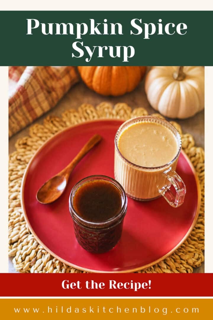 pumpkin spice syrup in jar beside cup of coffee, wooden spoon, and pumpkins.
