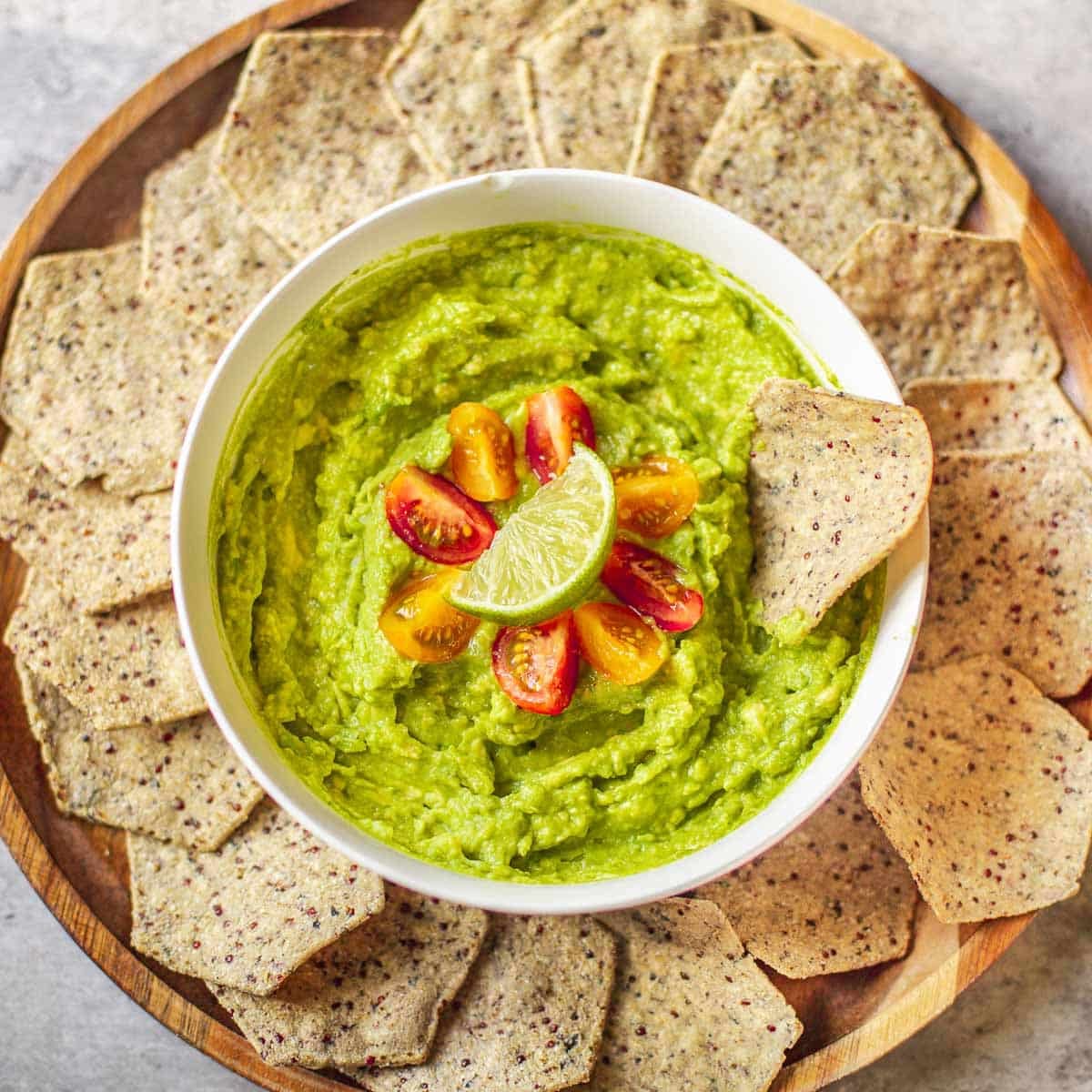 4 ingredient guacamole garnished with cherry tomatoes and lime surrounded by tortilla chips.