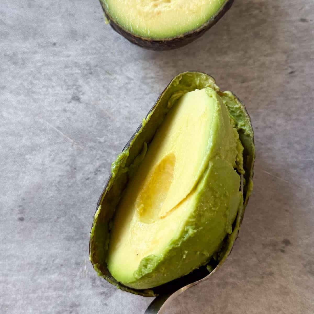 avocado flesh being scooped out with spoon.