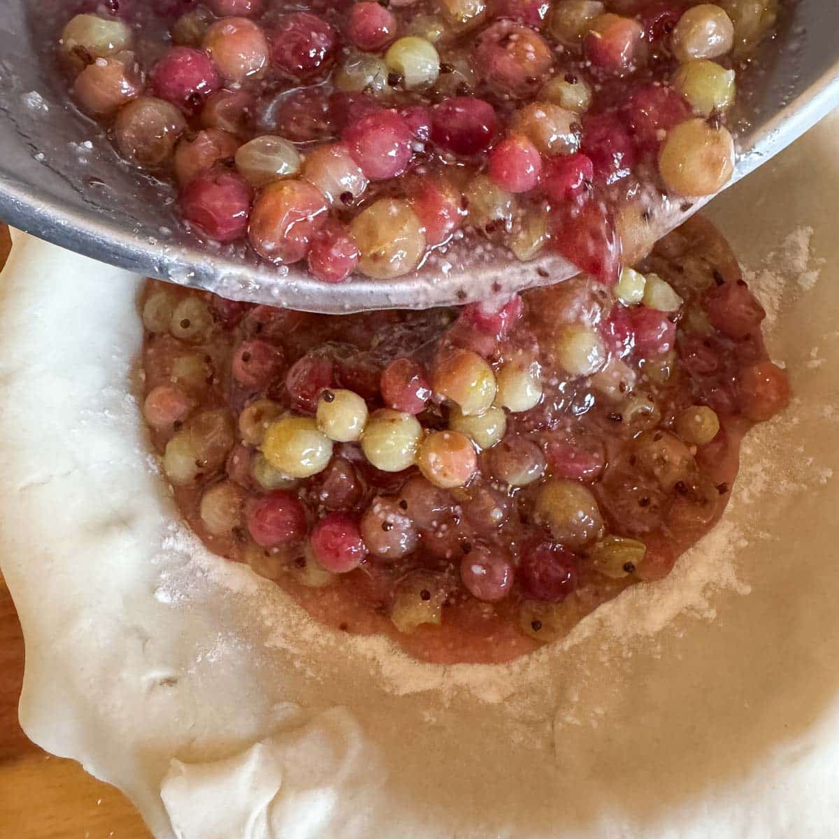 pouring gooseberry filling into a pie crust