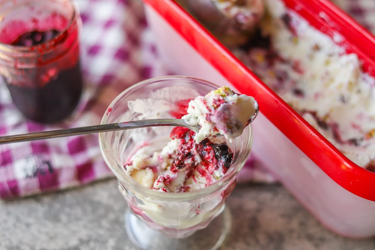 huckleberry ice cream in a glass cup with more ice cream and huckleberry sauce behind it