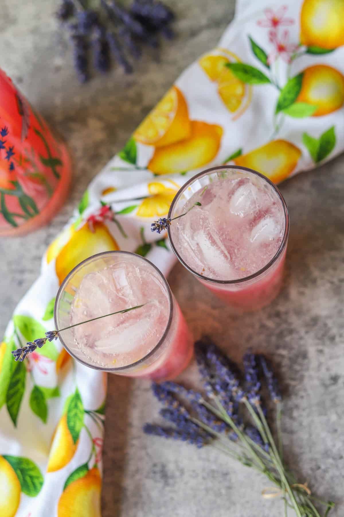 two glasses of lavender lemonade with a towel decorated with lemons and lavender sprigs