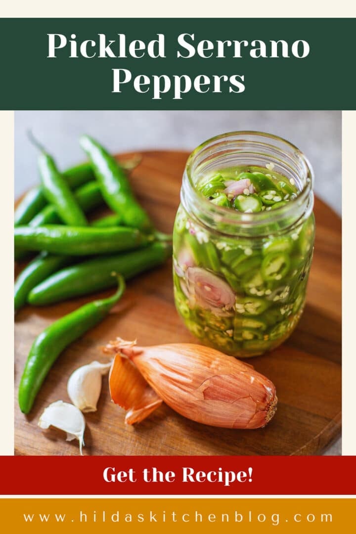 pickled serrano peppers in jar beside garlic, peppers, and shallots.