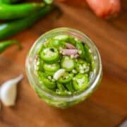 pickled serrano peppers in jar beside garlic, peppers, and shallots.