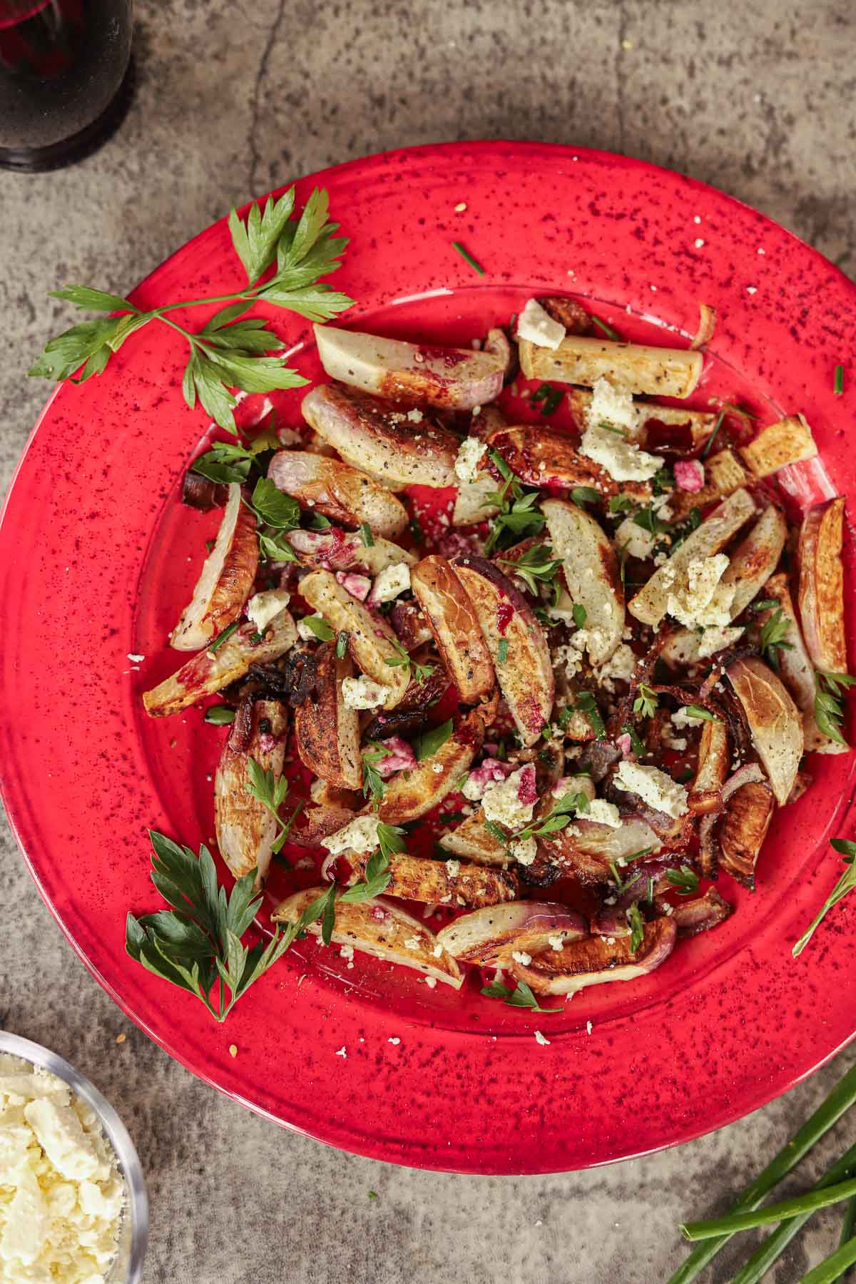 roasted turnips and onions on a red plate garnished with chopped parsley and chives