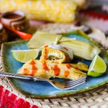 corn tamales with hot sauce and sour cream on a blue plate
