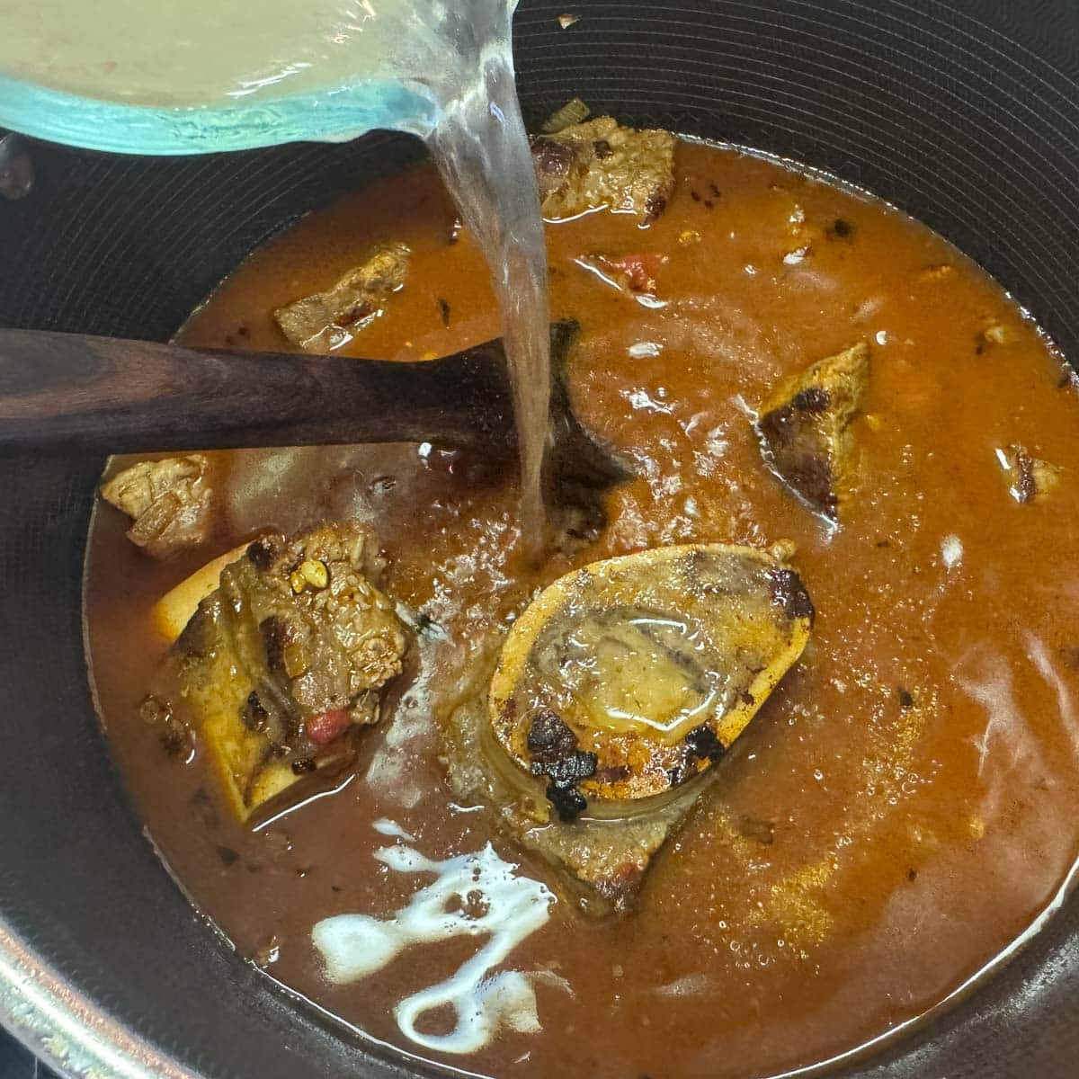 broth being added to a pot of fasolia
