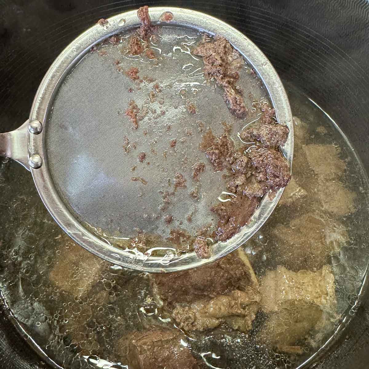 skimming scum from a pot with meat and water