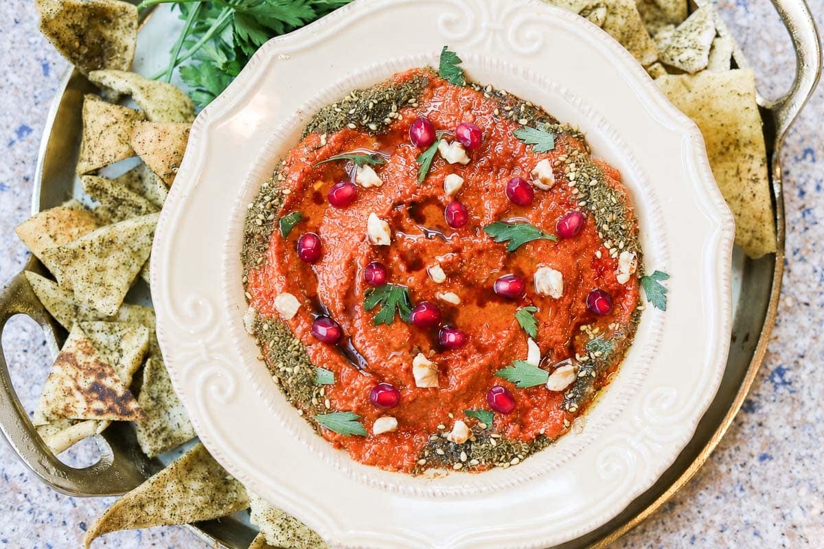 muhammara dip in a white bowl with pita chips around it