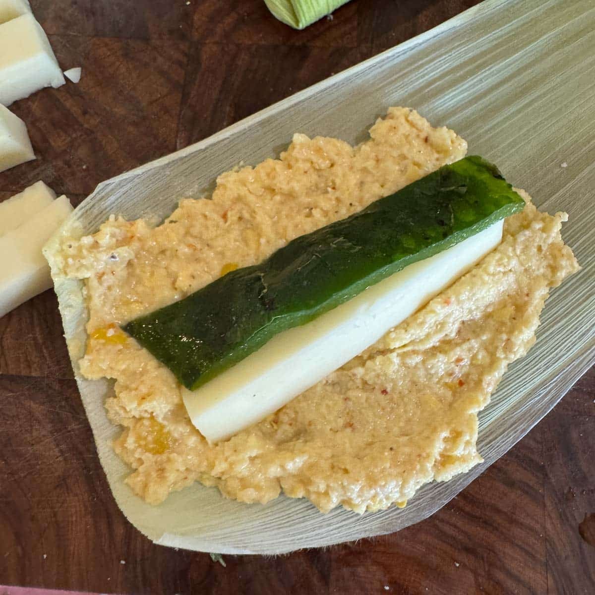 masa on a corn husk with a strip of cheese and a strip of poblano in the center of it