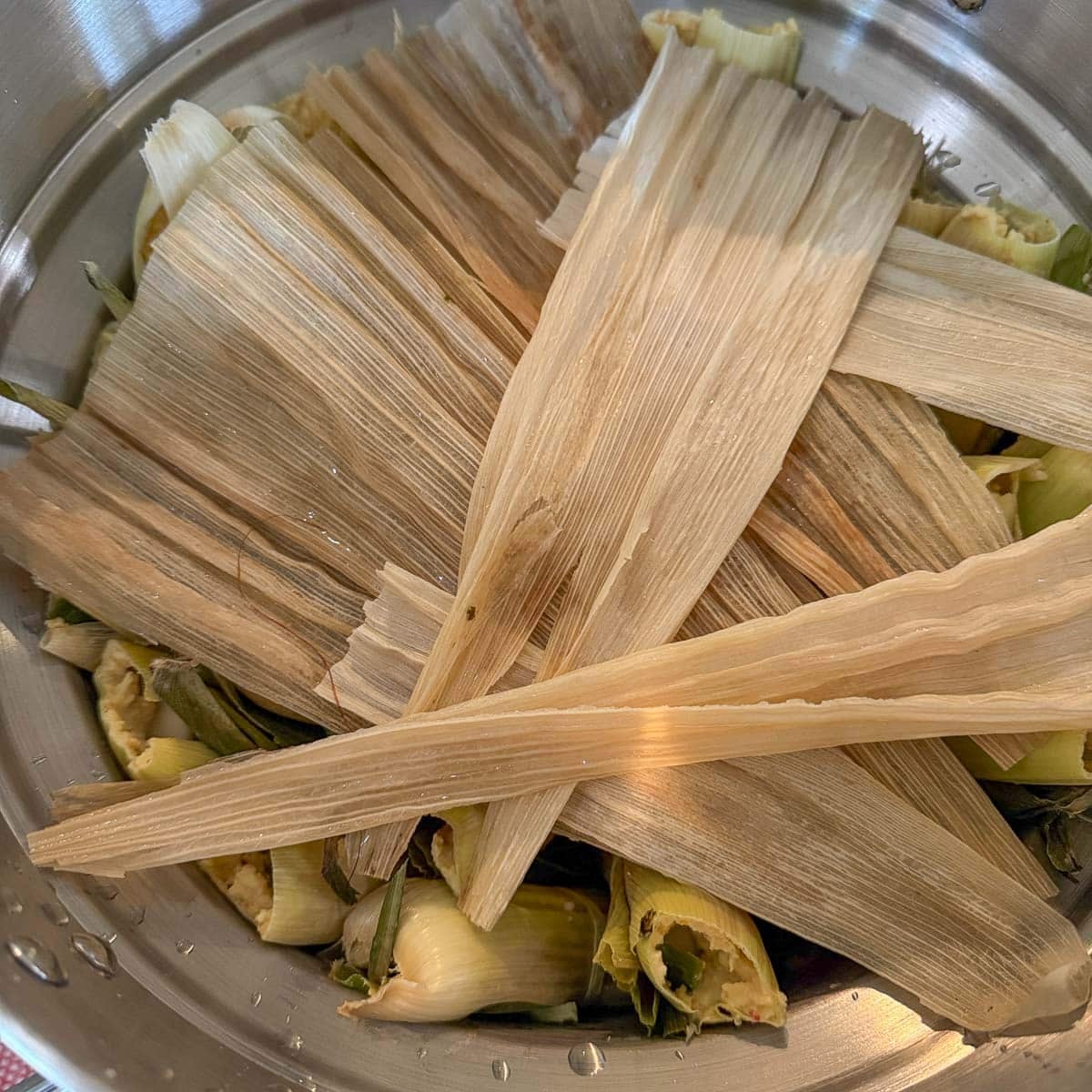 a pot of corn tamales with extra corn husks on top