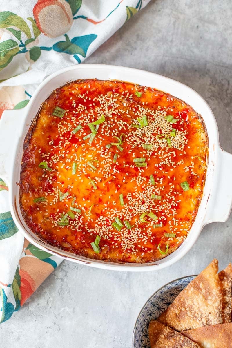 crab rangoon dip in baking dish beside bowl of wonton chips and dish towel.