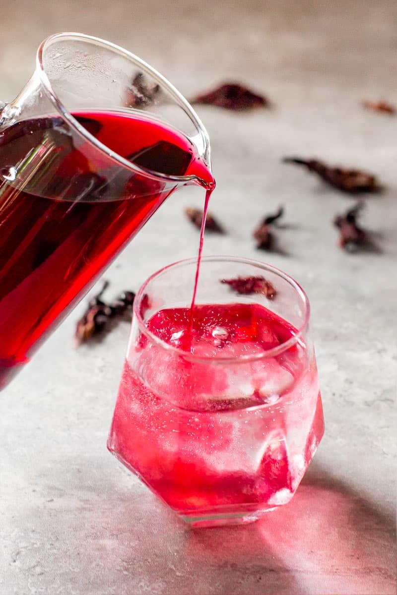 hibiscus simple syrup being poured into a carbonated drink.