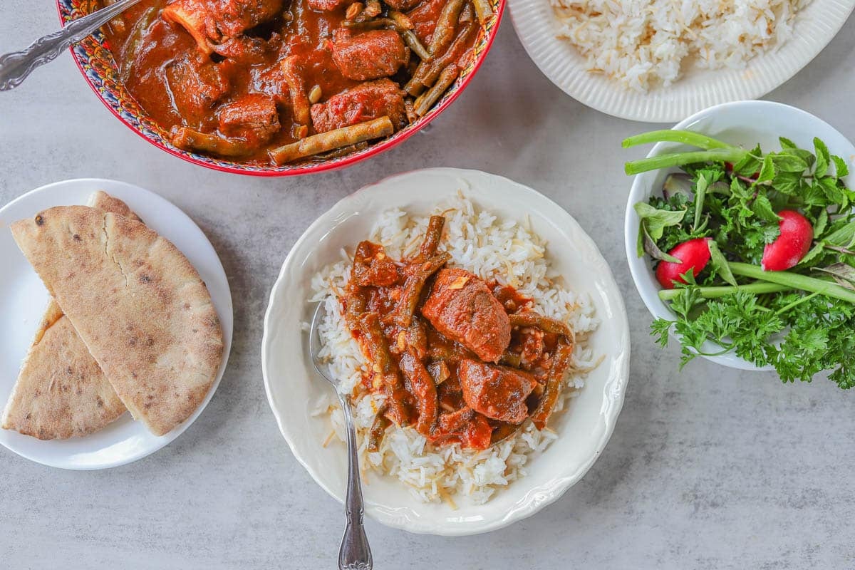 fasolia in a bowl and over white rice with fixings on the side