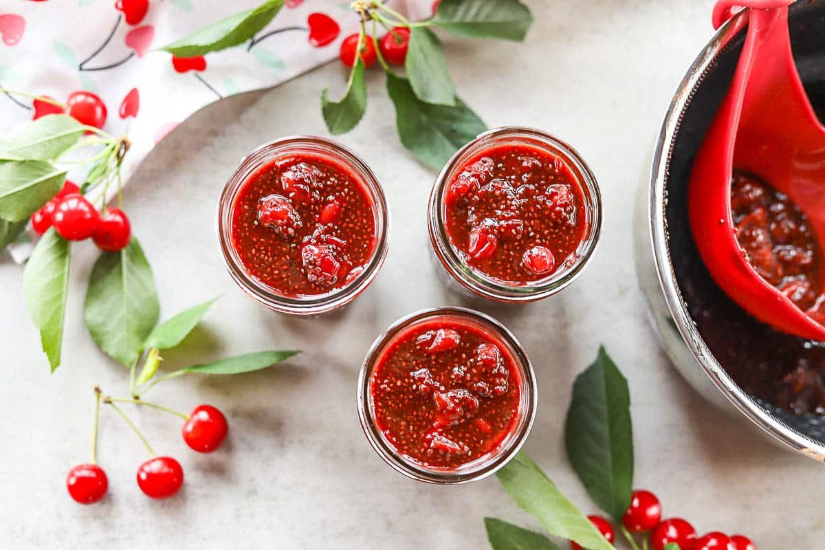 sour cherry chia seed jam in 3 jars with cherries around them
