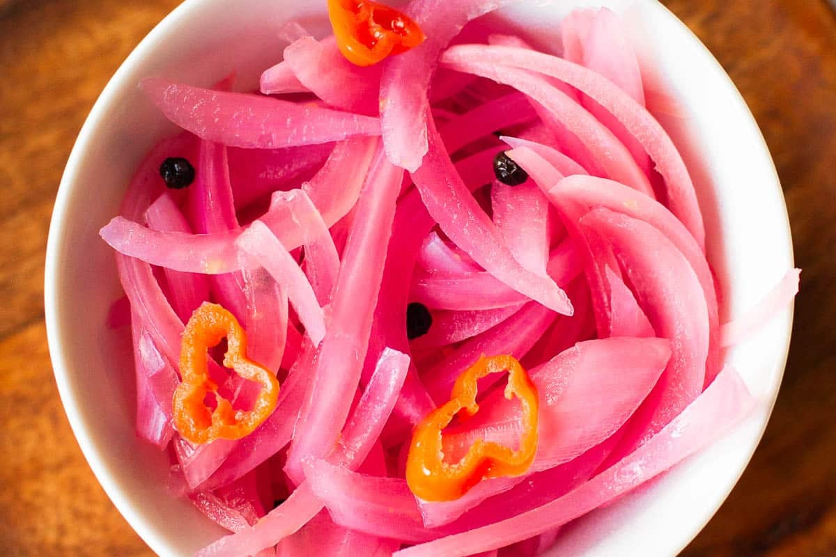 quick pickled red onions in bowl with peppercorns and habanero slices.