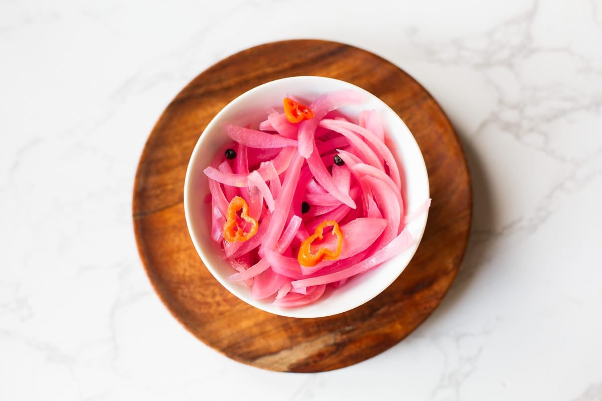 quick pickled red onions in bowl with peppercorns and habanero slices.
