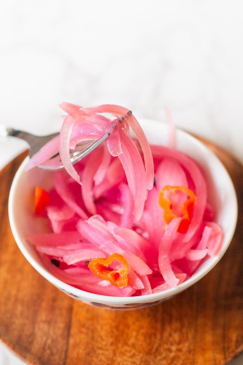 fork holding quick pickled red onions over bowl.