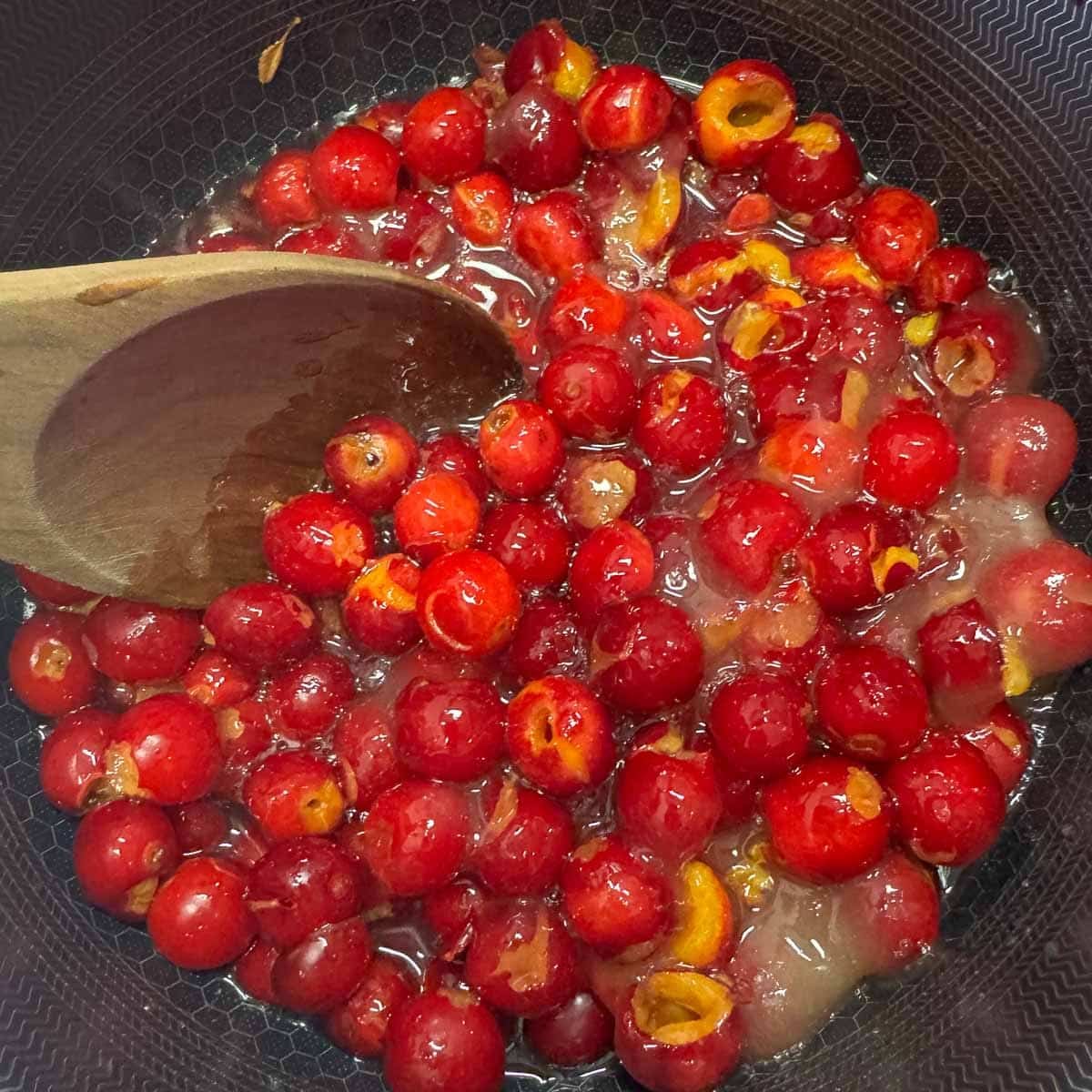 sour cherry jam being stirred with a wooden spoon
