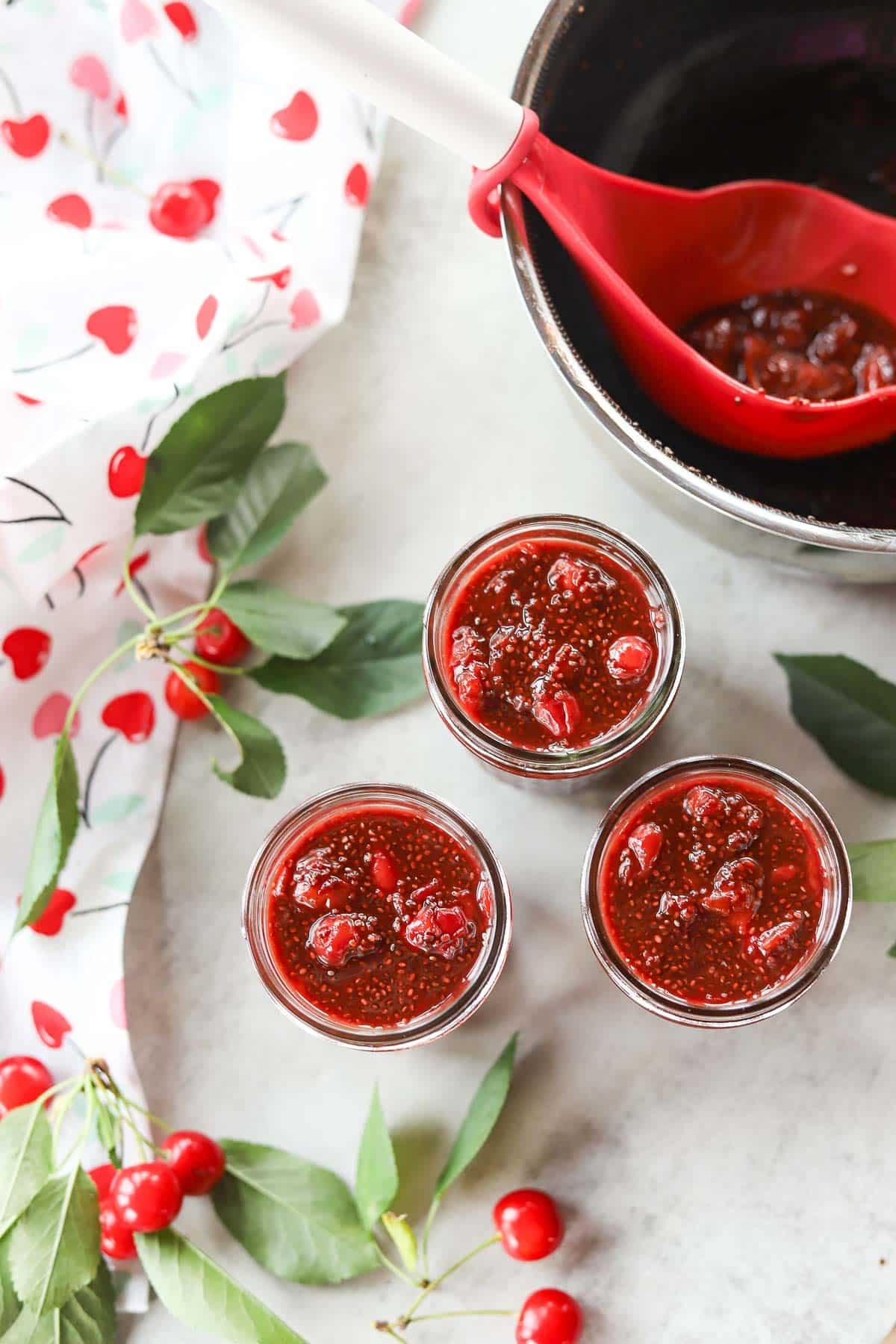 3 jars sour cherry chia jam with cherries around it