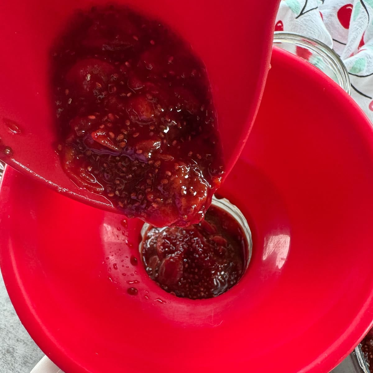ladling sour cherry jam into jars through a red funnel