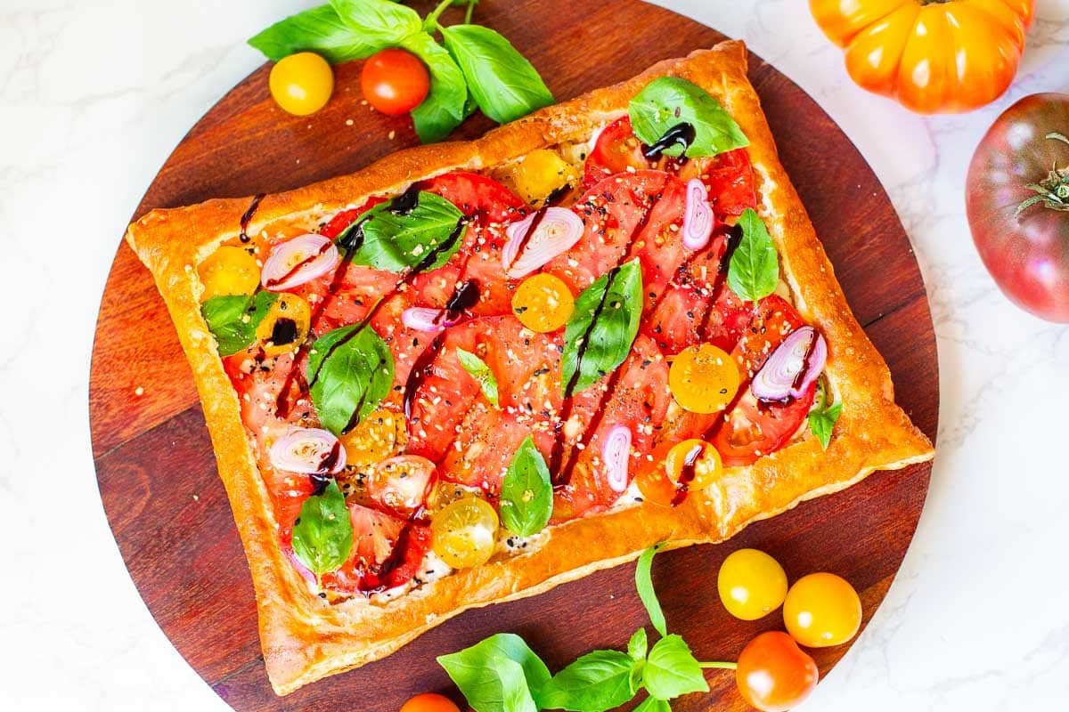 puff pastry tomato tart surrounded by tomatoes and basil.