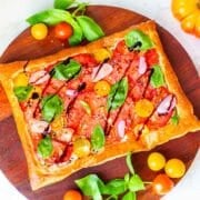 puff pastry tomato tart surrounded by tomatoes and basil.