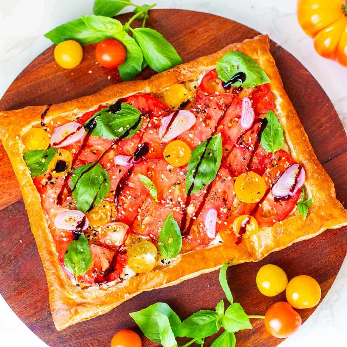 puff pastry tomato tart surrounded by tomatoes and basil.