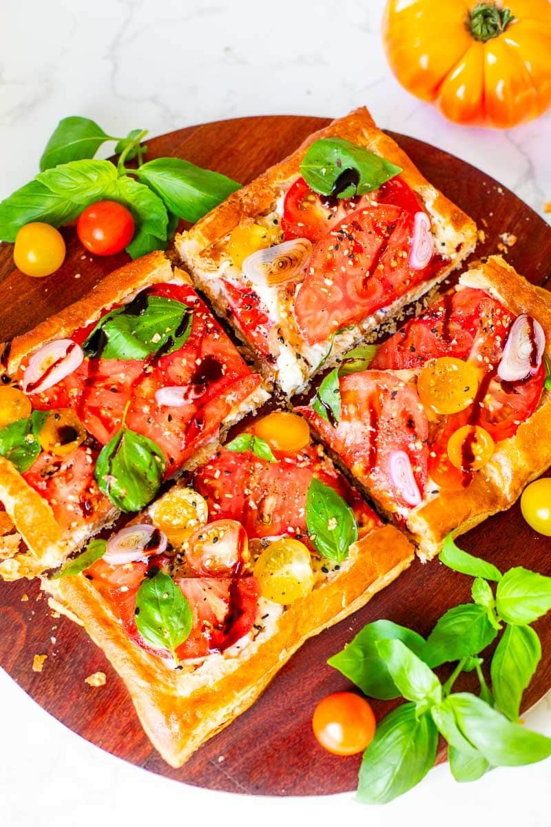 tomato tart with puff pastry surrounded by tomatoes and basil.