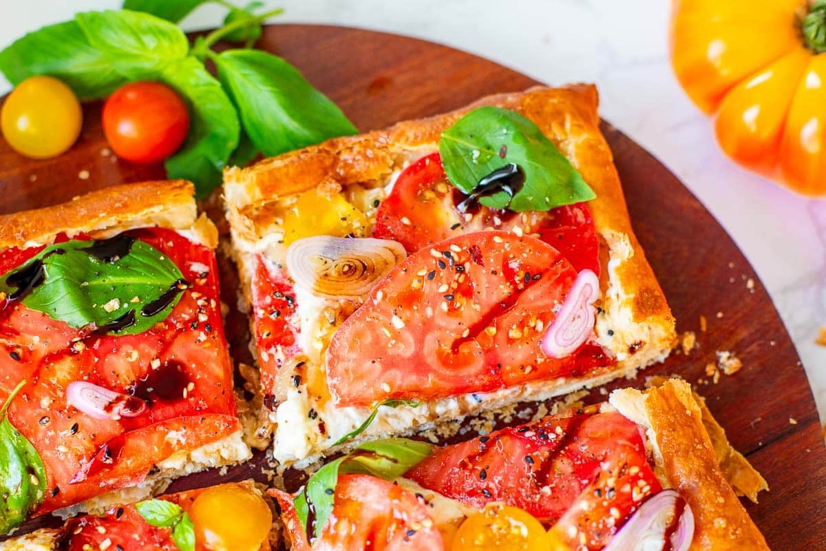 sliced tomato tart using puff pastry beside tomatoes and basil.