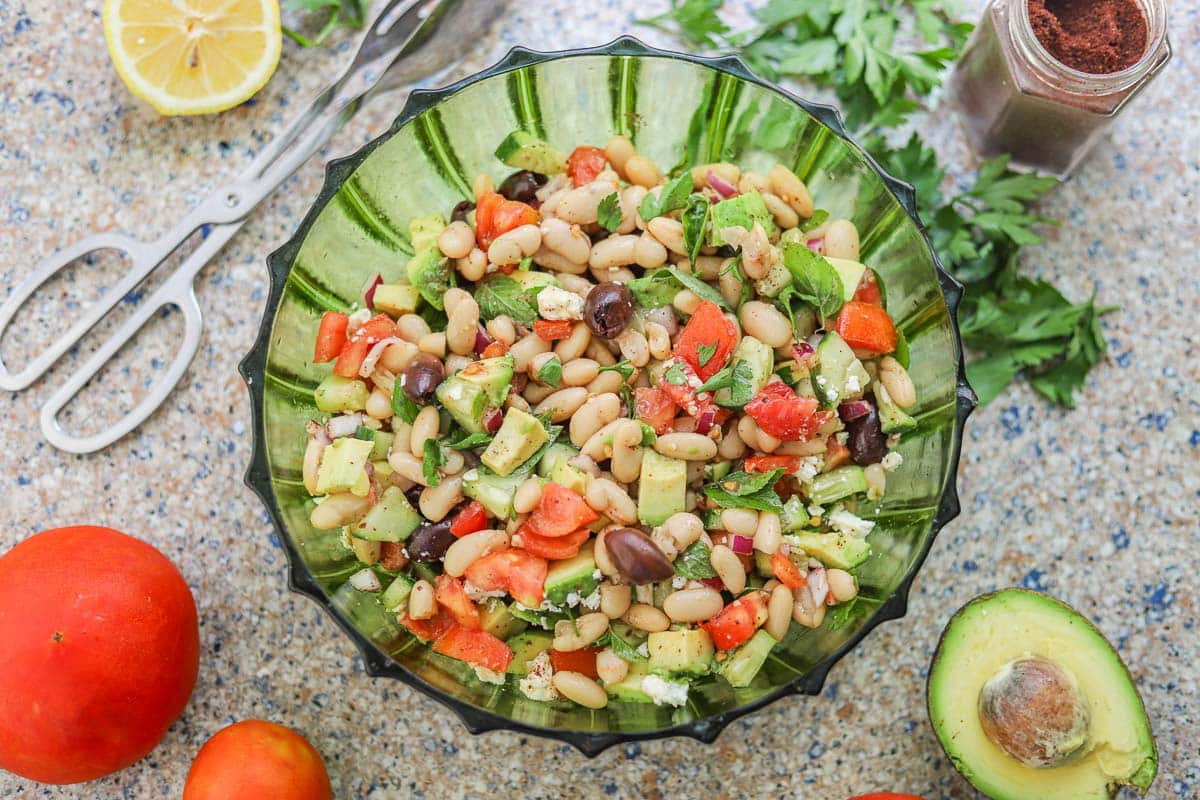 white bean salad with veggies, tongs, and sumac in a jar around it,