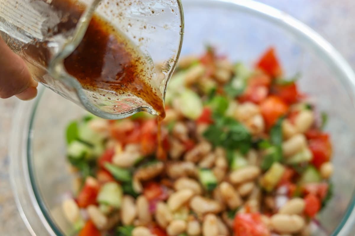 bean salad in a bowl with salad dressing being poured over it
