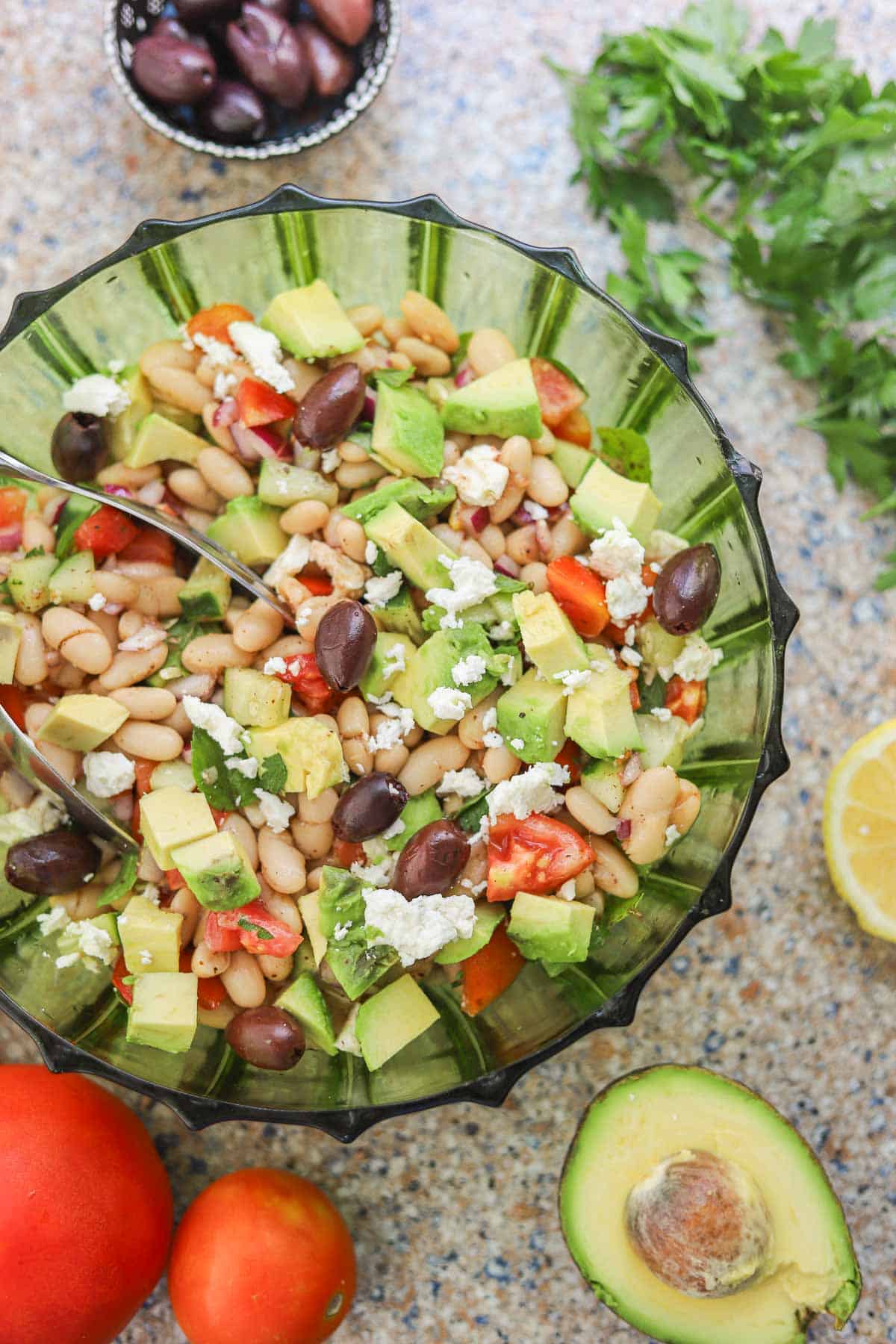 white bean salad in a green salad bowl with veggies around it.