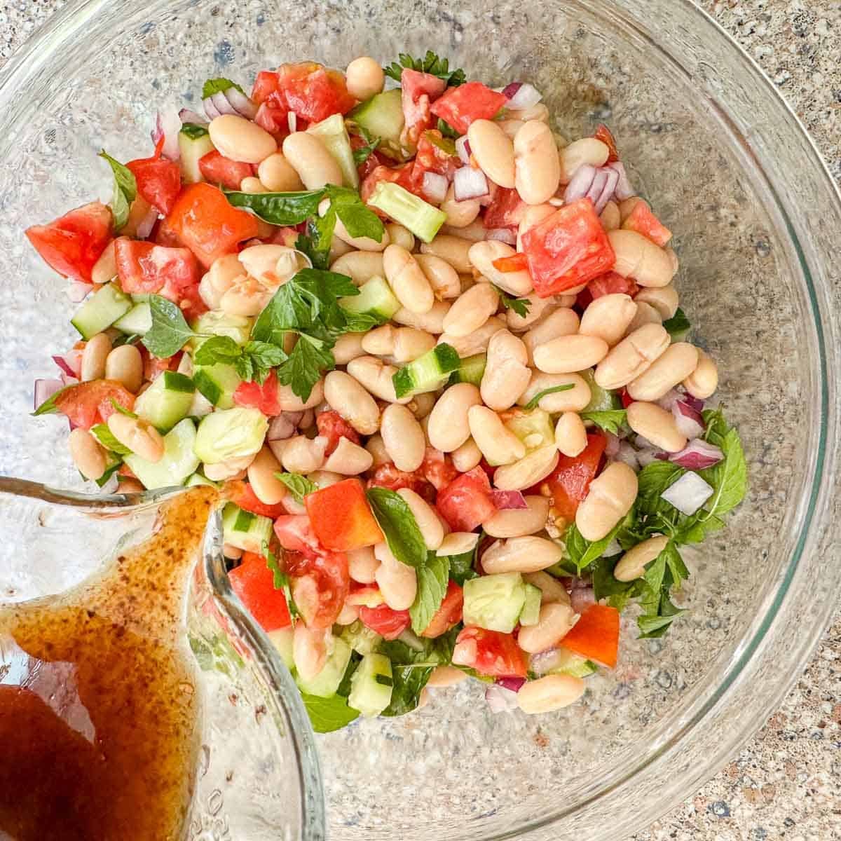 salad dressing being poured over a bean salad