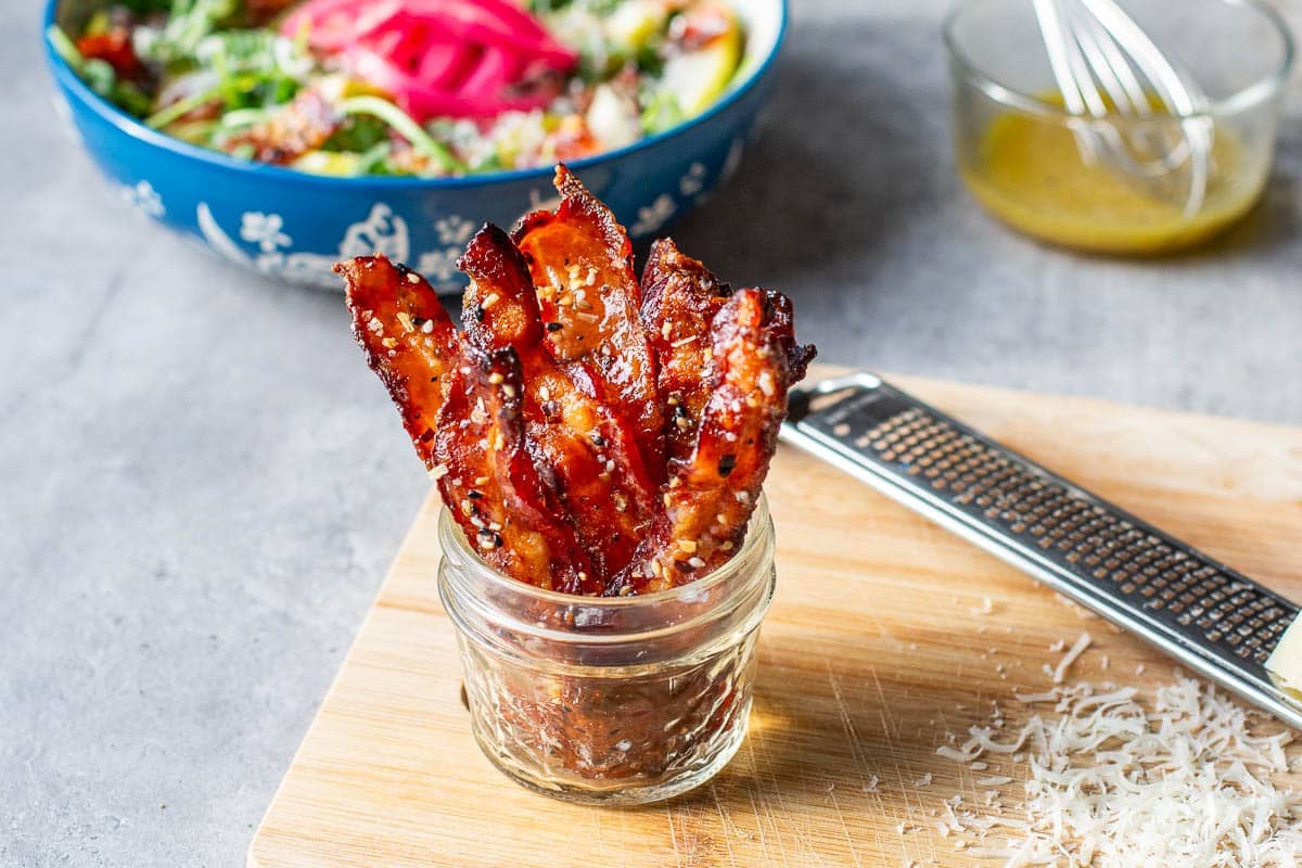 candied bacon in a jar with a salad behind it